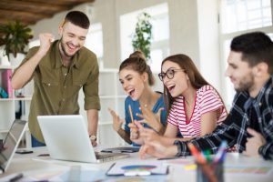 young emotional business people joyfully working on laptop together group of laughing men and women spending time at work in modern cozy office scaled e1660734263885